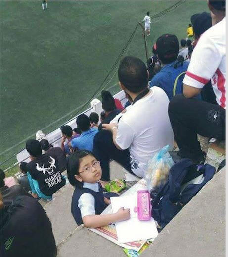 Daddy enjoys a football match while kiddo does homework. (Mizoram, India)